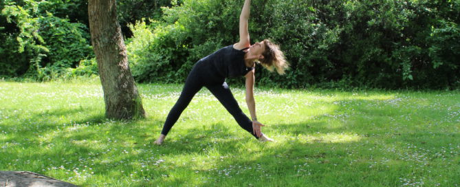 En kvinde står i en Yogastilling i museets sommergrønne park