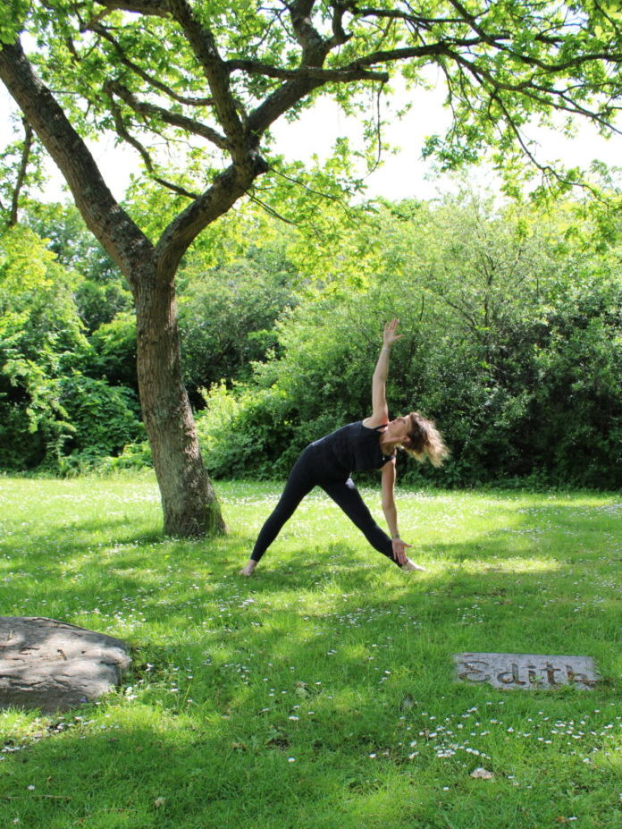 En kvinde står i en Yogastilling i museets sommergrønne park