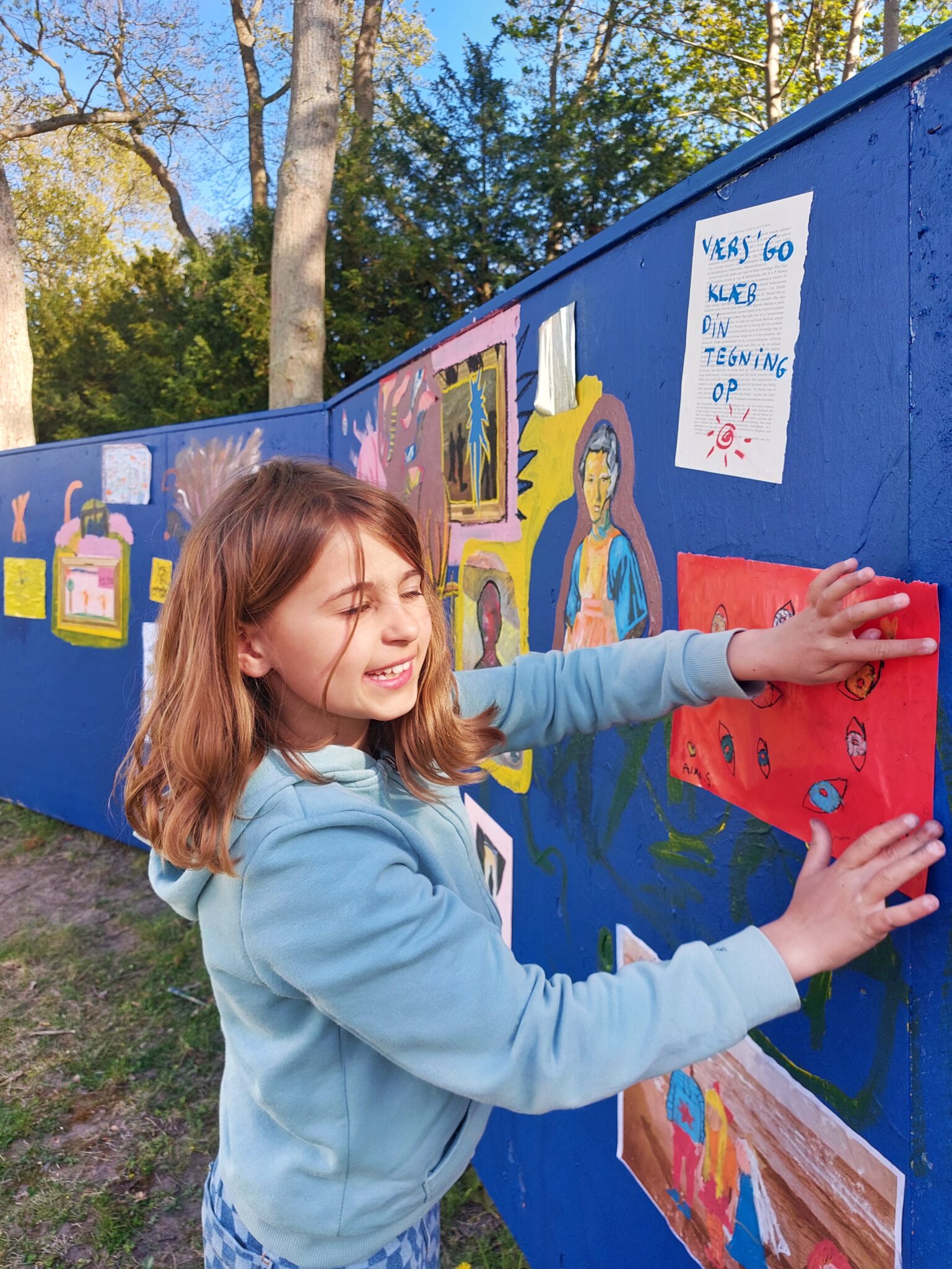 Et barn sætter sin tegning op på et blåt stakit