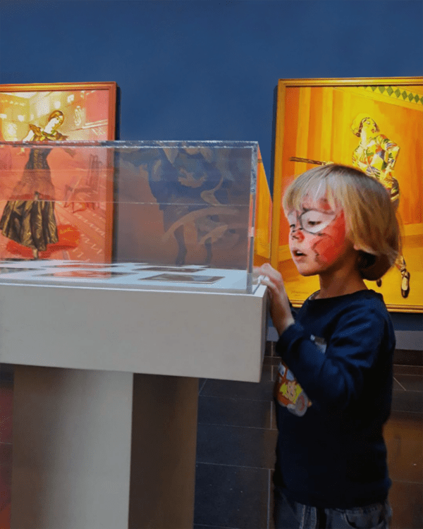 Et barn med rød Spiderman-ansigtsmaling kigger på kunst i en montre,